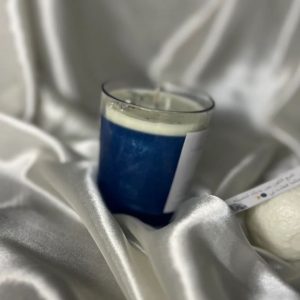 شمعة زرقاء داكنة مزينة بنجوم وكوكب فضي، مستوحاة من سماء الليل، موضوعة على قماش ساتان ناعم